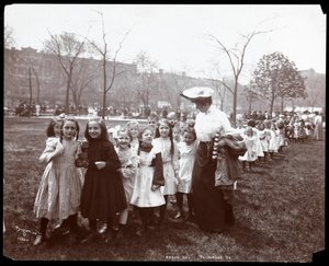 Children in a long line being led by a woman on Arbor Day at Tompkins Square Park, New York, 1904